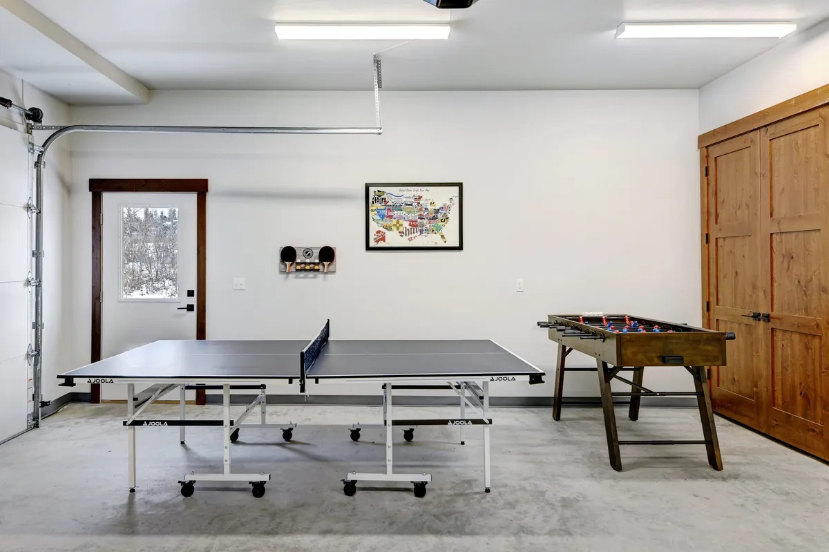A vibrant rec area featuring both a ping pong table and a foosball table, with people actively playing and socializing. The space is filled with energy, laughter, and casual gathering, with a doorway and framed map in the background adding visual interest.