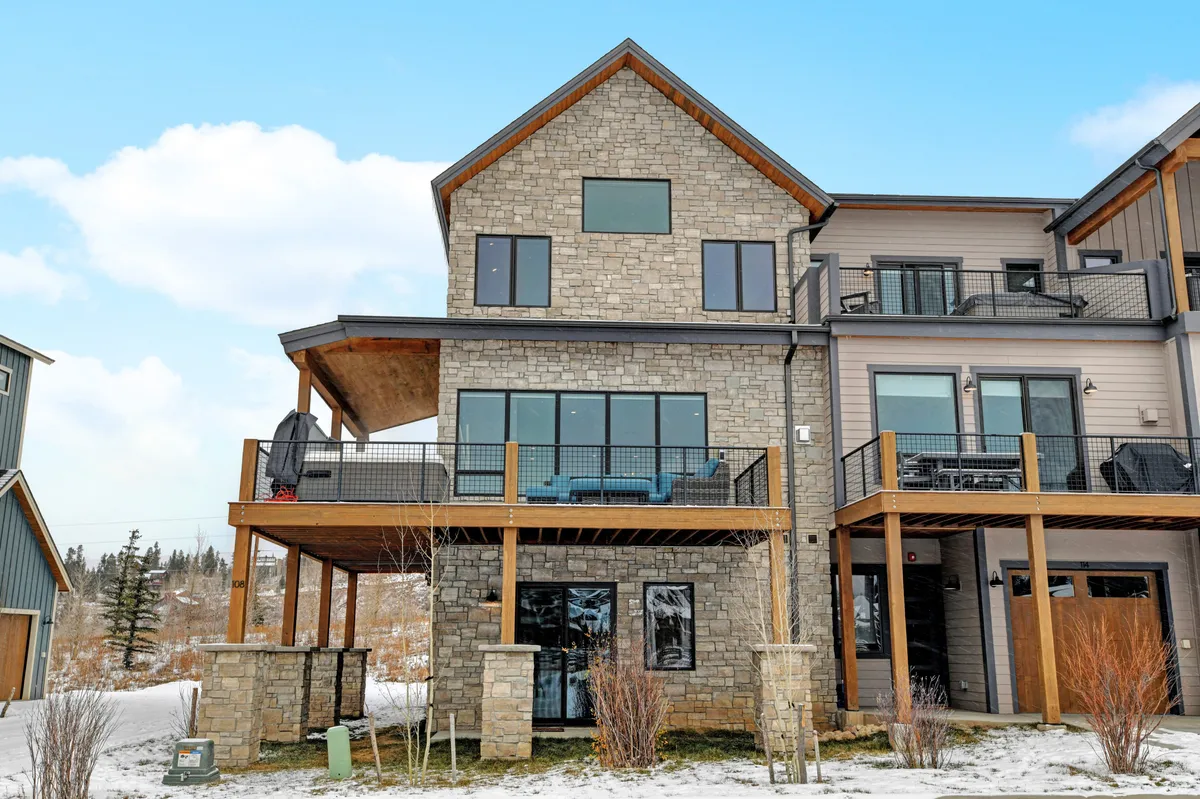 An exterior view of Villa 108’s stone facade, balconies, large windows, and a spacious deck area. The inviting setup hints at gatherings, sunset views, and the mountain scenery, bridging the comfort of home with the natural environment.