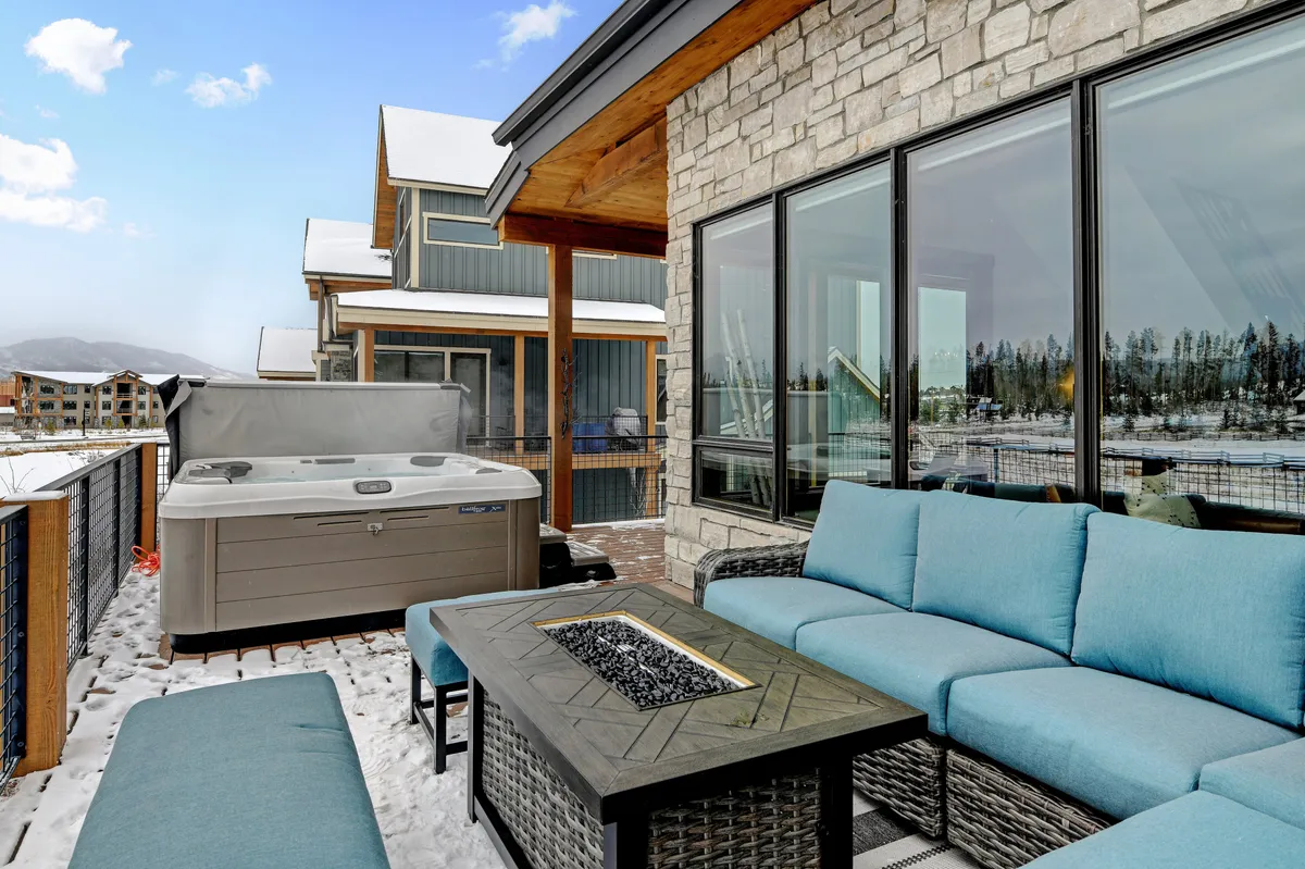 A luxurious outdoor area pairs a steaming hot tub with a cozy seating arrangement around a modern fire table, all set to take advantage of mountain views and fresh air. Even in winter, the space feels welcoming and perfect for hosting friends and family.