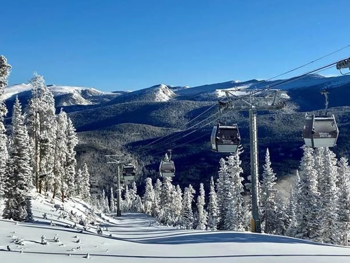 A stunning exterior view featuring a ski lift gliding above snow-covered trees, with a majestic mountain range in the background. The fresh powder and clear sky create an inviting landscape for winter sports enthusiasts.