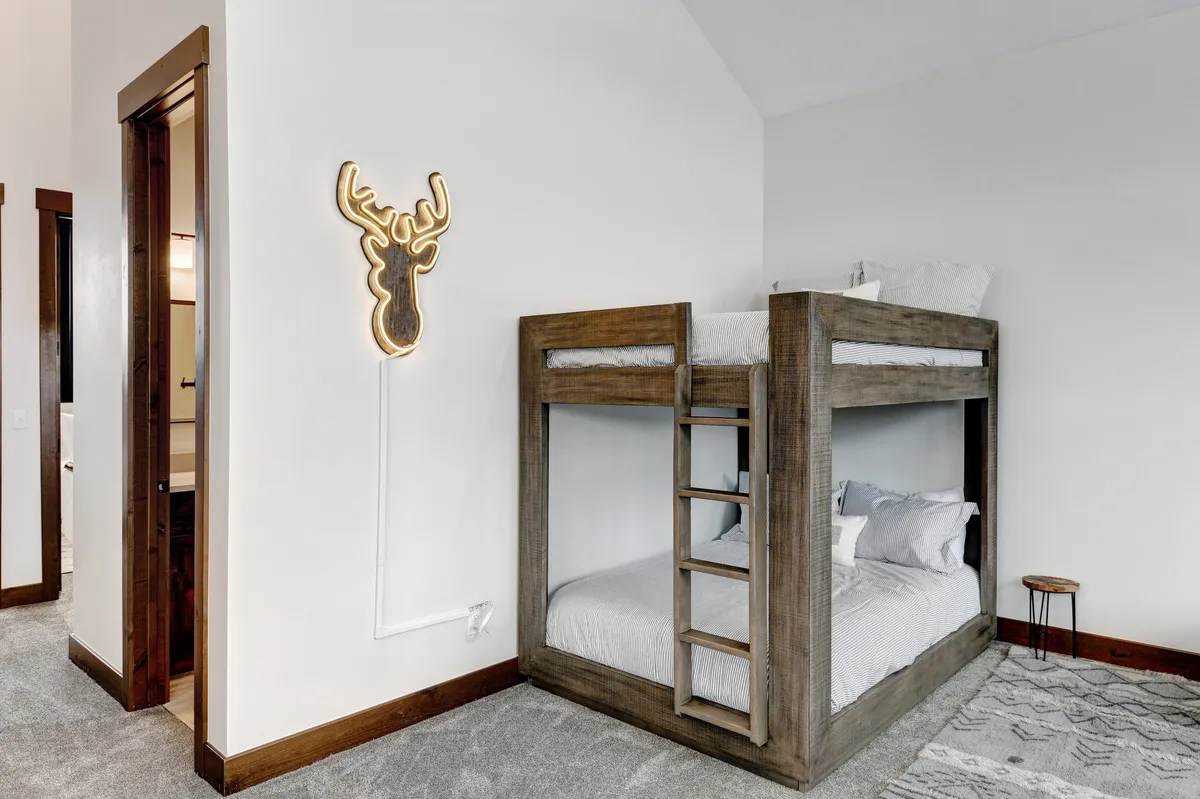 A cozy custom bunk room highlighted by a bunk bed, whimsical deer-themed light fixture, and a textured rug. The playful, inviting atmosphere makes it ideal for children and teens seeking their own fun retreat.