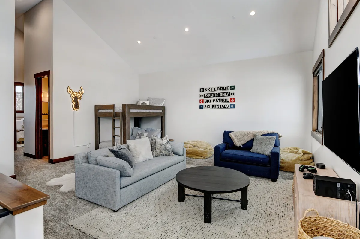 A welcoming lofted rec area with a comfy sofa, built-in bunk beds, a ski lodge sign, and a television. The space invites relaxation, socializing, and game time, making it perfect for mixed-age groups or family gatherings.